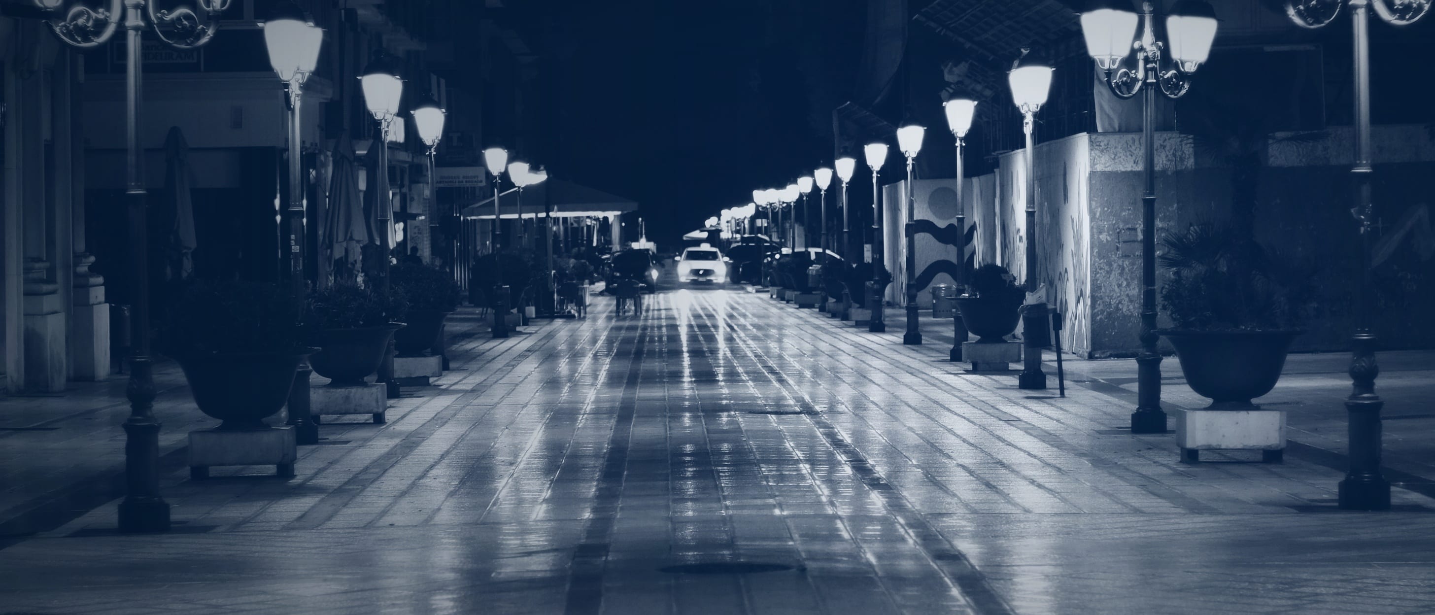A pedestrian street at night with wet paving and two rows of glowing street lamps - nobody is recognisable.