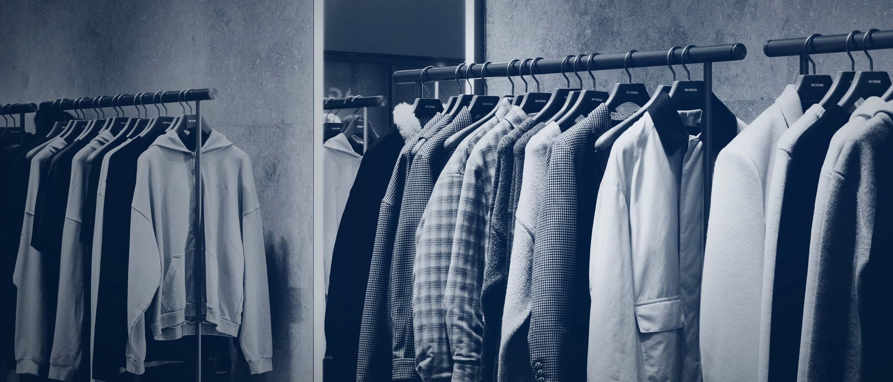 Clothing rails with jackets and sweaters against a concrete wall in a store.