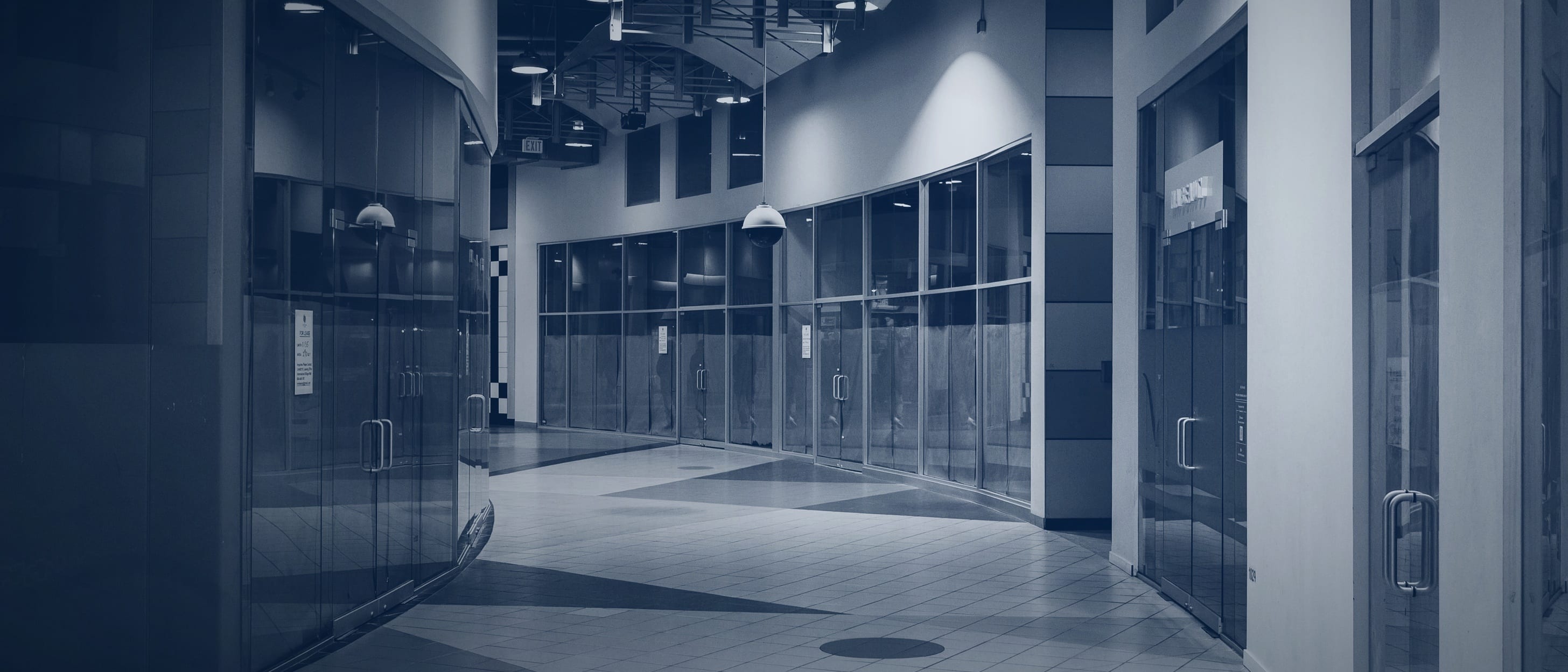 An empty shopping passage with glass shopfronts and a patterned tile floor - nobody is shown.