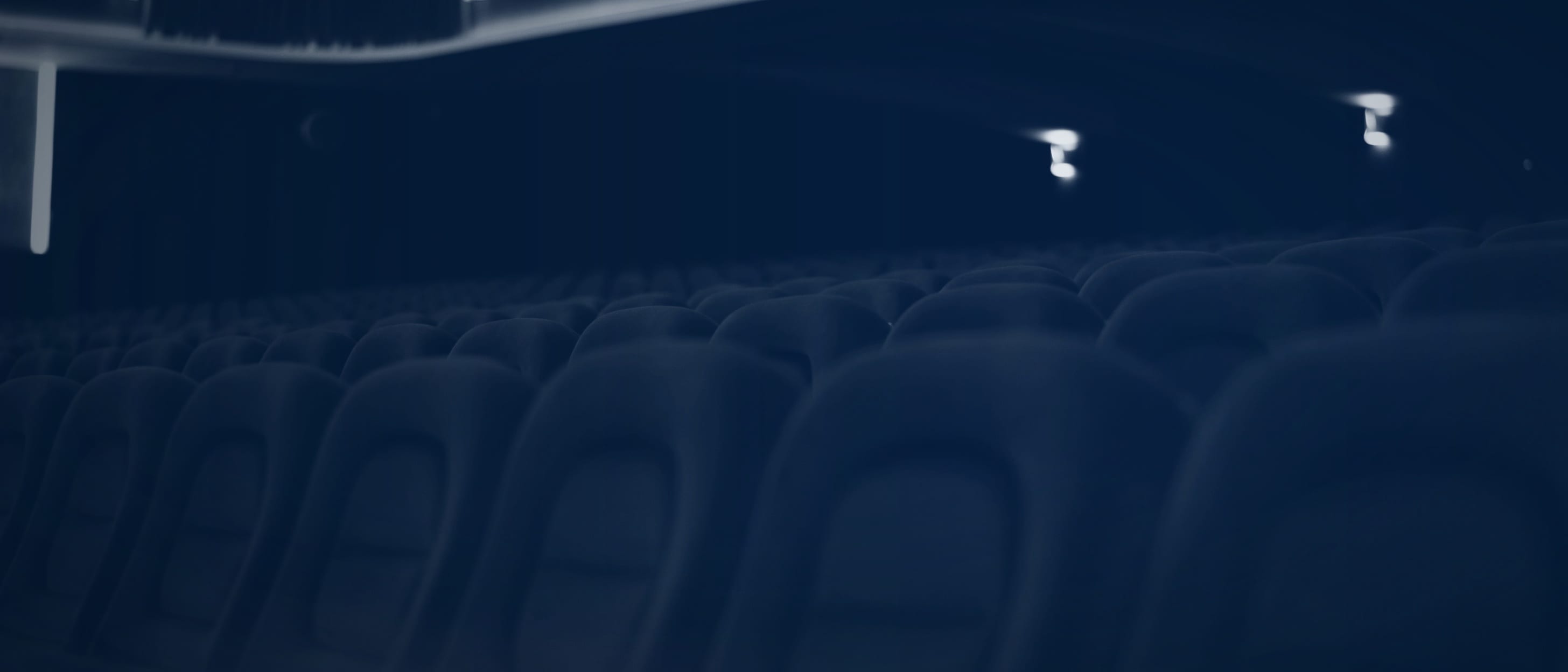 Empty padded rows of seats in a darkened cinema auditorium with a lit balcony - nobody is shown.