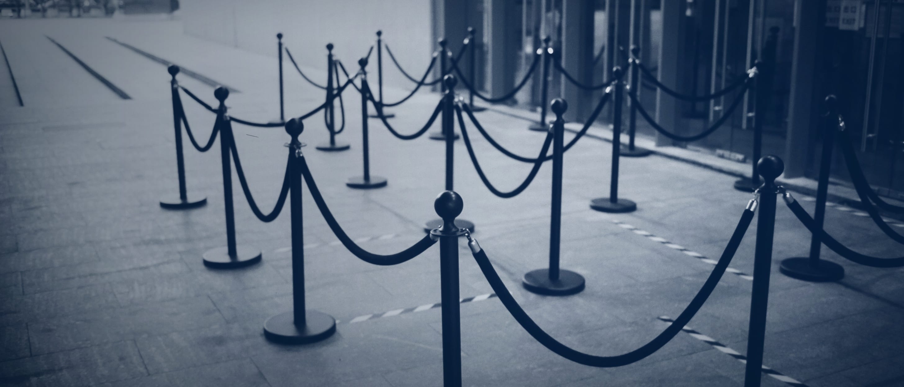 An empty queue line of posts and ropes in front of a building entrance - nobody is shown.