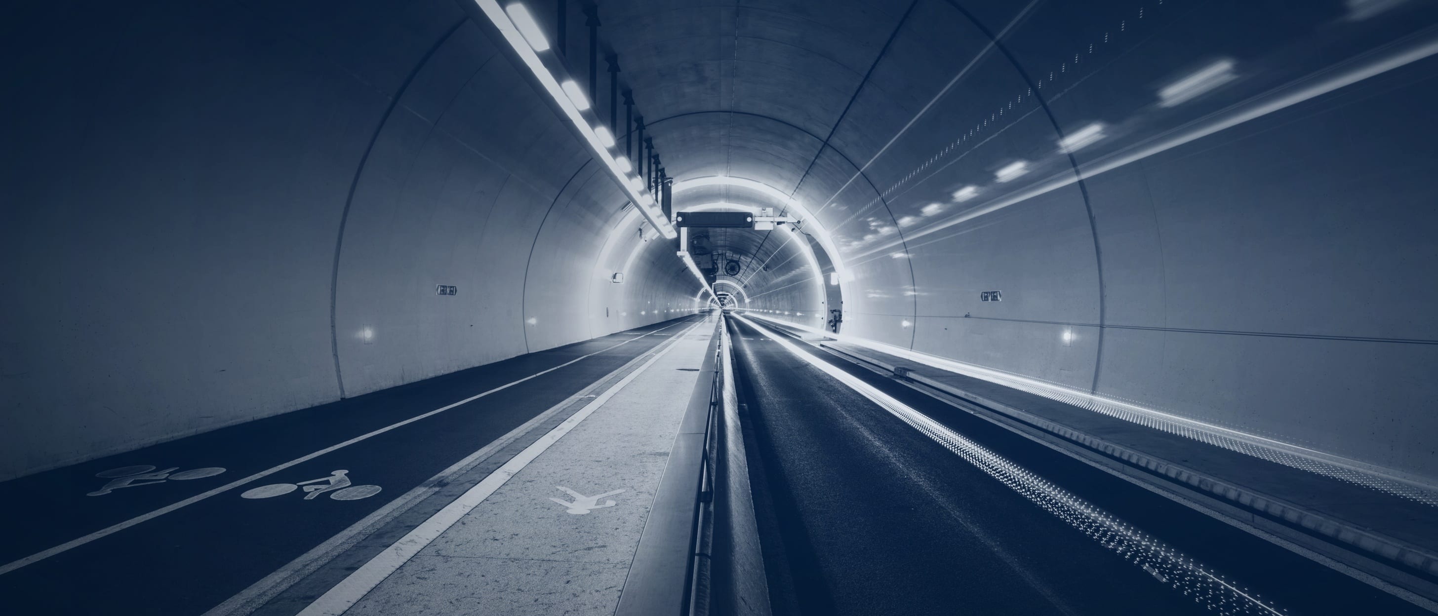 A long tunnel with a footpath and cycle lane, light trails running towards a bright point in the distance - nobody is shown.
