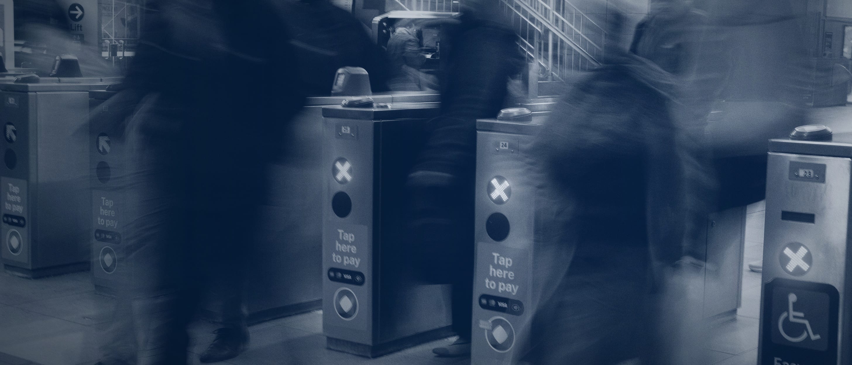 People blurred in motion passing through access gates, signals lit on the devices - no individual is identifiable.