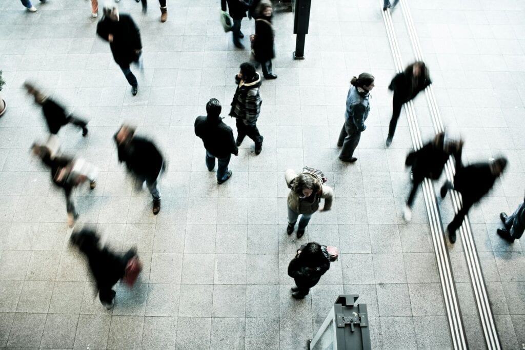 Menschen bewegen sich durch eine Bahnhofshalle, von oben aufgenommen, mit Bewegungsunschaerfe. Einzelne Personen sind nicht erkennbar.