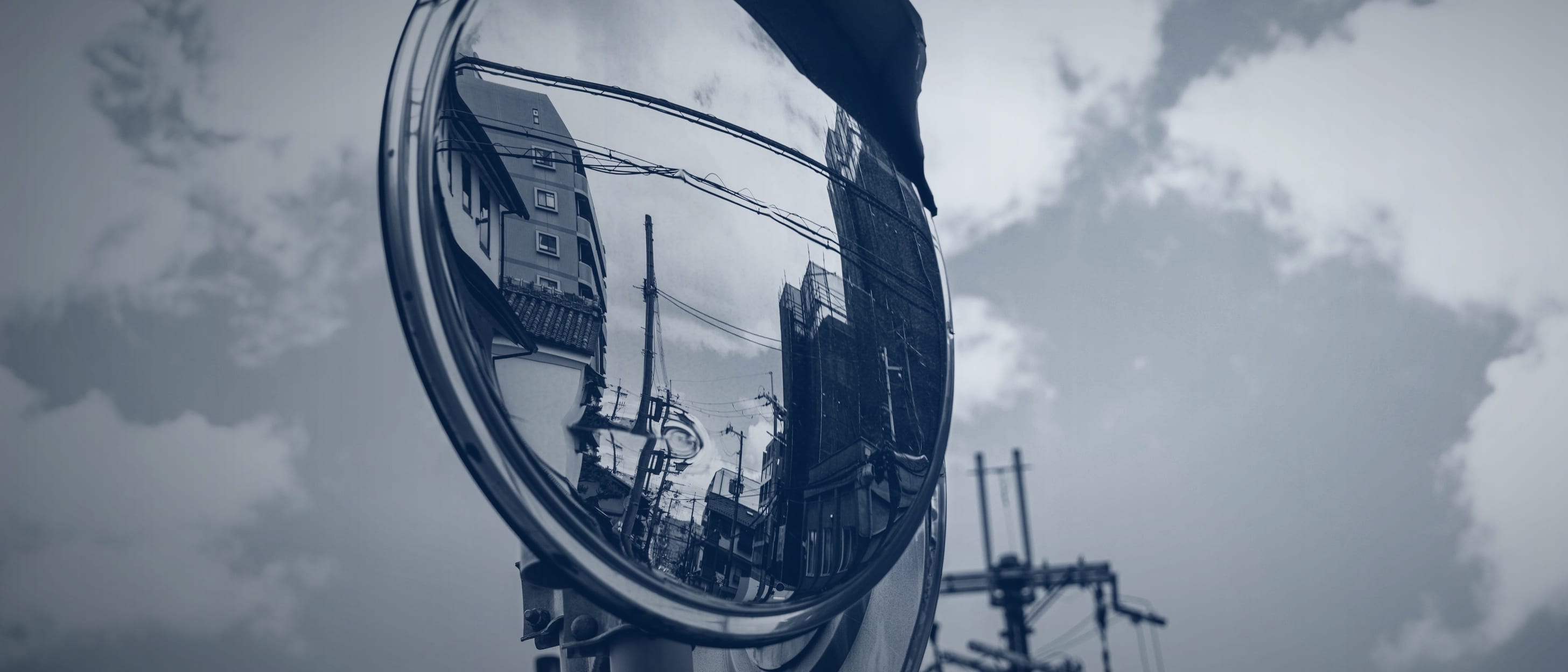 A round traffic mirror against a cloudy sky, reflecting buildings and utility poles - nobody is shown.